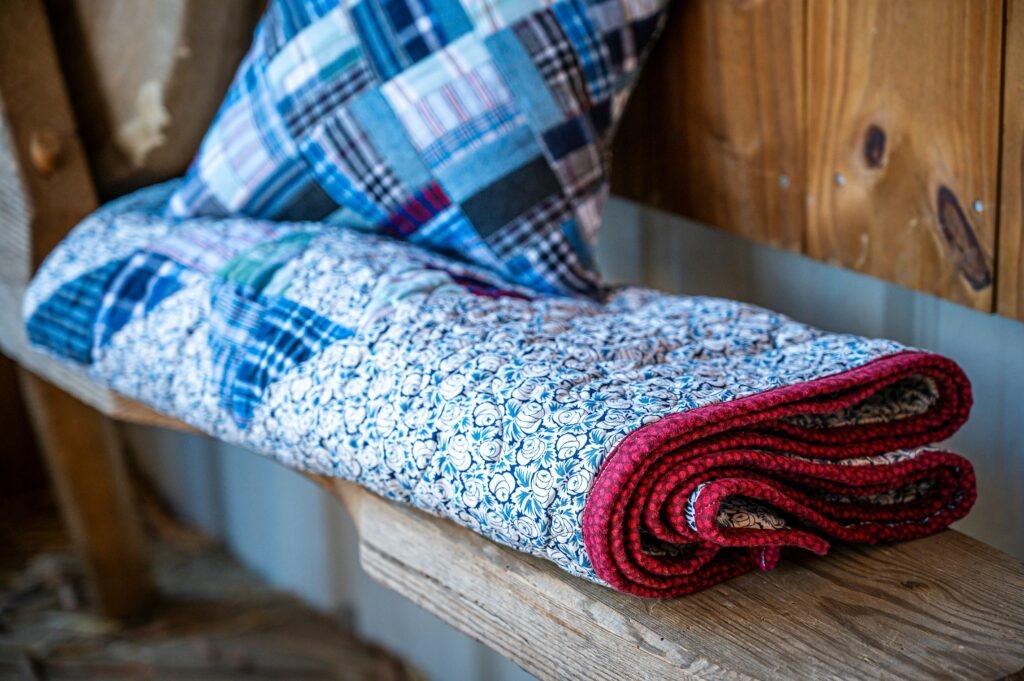 A quilt and pillow are resting on a wooden shelf.